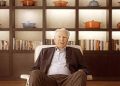 Paul van Zuydam seated in front of cookware and books, reflecting his legacy as Le Creuset’s visionary leader.